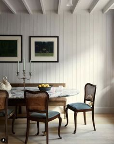 a dining room table with four chairs and two pictures on the wall above it,