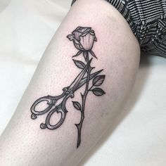 a black and white photo of a rose with scissors on the side of a woman's leg