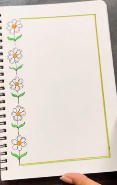 someone is holding up a notebook with flowers on the page and green trimmings