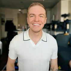 a man in a white shirt is smiling at the camera and has tattoos on his arms