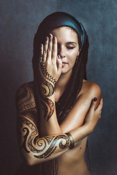 a woman with tattoos on her arms and chest holding her hand up to her face