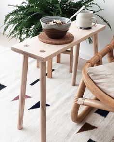 two wooden tables with bowls on them in front of a potted plant and chair