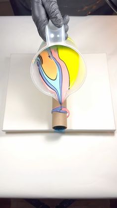 a person in black gloves pours colored liquid into a vase on a white surface