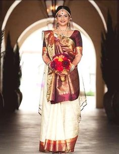 a woman in a white and gold sari with flowers on her head standing next to an archway