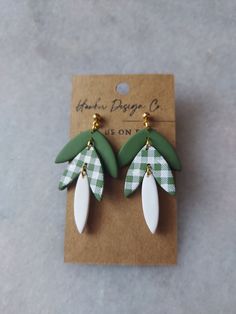 two green and white leaf shaped earrings on top of a card