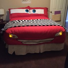 a red bed with two eyes on it and a checkered bedspread in the shape of a car