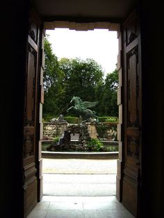 an open door leading to a garden with a statue in the center and trees behind it