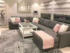 a living room with grey couches and pink pillows on the rug, white coffee table