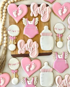 baby shower cookies decorated with pink and white icing on a wooden tray next to beads