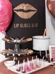 the lip gloss bar is set up with pink and gold balloons, candles, and other items