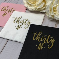 three napkins with gold foil lettering on them and some white flowers in the background