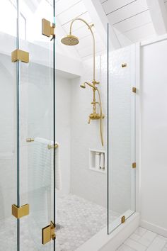 a bathroom with a glass shower door and white tile flooring that has gold fixtures