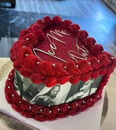 a heart shaped cake with red frosting and hearts on the top is sitting on a table