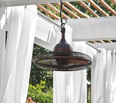 an outdoor light hanging from the side of a pergolated area with white drapes