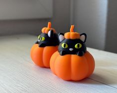 two small plastic pumpkins with black cats on them sitting on a table in front of a window