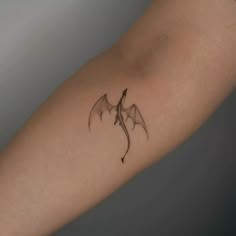 a small tattoo on the arm of a woman with a dragon wing in black ink