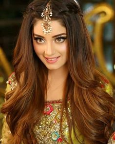 a woman with long brown hair wearing a headpiece and gold dress is smiling at the camera