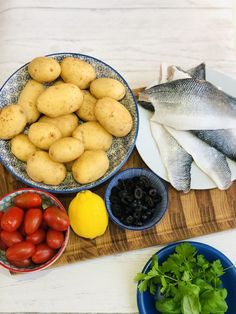 fish, potatoes, olives and tomatoes on a cutting board next to other foods