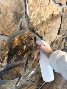 a person using a spray bottle to paint a stone wall