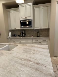 a kitchen with white cabinets and marble counter tops