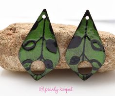 a pair of green and black leaf shaped earrings sitting on top of a piece of rock