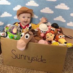 a baby sitting in a cardboard box filled with toy animals and other toys on the floor