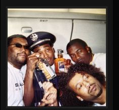 four men pose for the camera while one man drinks from a bottle