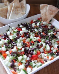 a white dish filled with black olives, cucumber and other vegetables next to tortilla chips