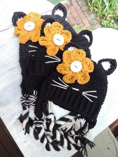 two crocheted hats with cats on them sitting on top of a wooden table