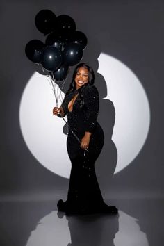 a woman in a black dress holding balloons and posing for a photo with the moon behind her