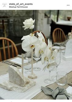 the table is set with white flowers and place settings