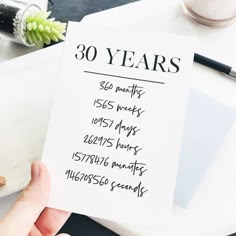 a person holding up a piece of paper with the date 30 years written on it