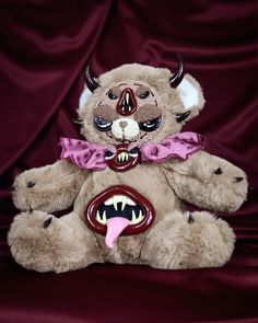 a stuffed animal with horns and fangs on it's face, sitting in front of a maroon background