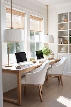 two laptops sitting on top of a wooden desk in front of three white chairs