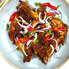 a white plate topped with meat covered in red onions and cilantro peppers next to chopsticks