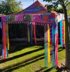 a colorful tent with ribbons hanging from it's sides in the grass near a tree