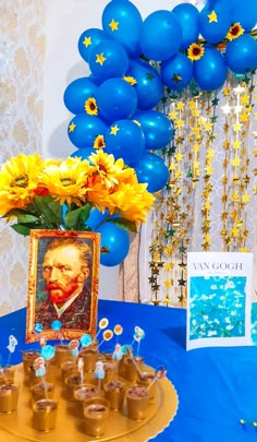 a blue table topped with cupcakes and yellow flowers next to a vase filled with sunflowers