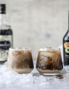 two glasses filled with ice sitting next to bottles