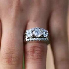 a woman's hand with two wedding rings on her left and the other hand holding an engagement ring