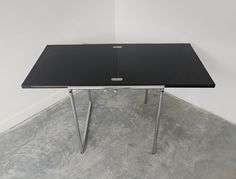 a black table sitting on top of a cement floor next to a white wall in an empty room