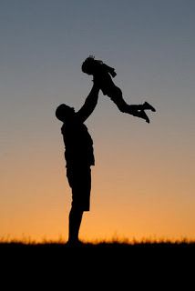 the silhouette of a man holding a child in his arms, with an orange and blue sky behind him