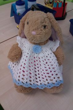 a stuffed animal wearing a crocheted dress sitting on a wooden table next to other toys