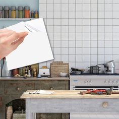 a person holding up a piece of paper over a kitchen counter with an oven and stove in the background