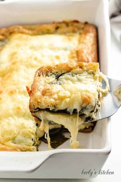 a casserole dish with cheese and spinach being lifted from the casserole