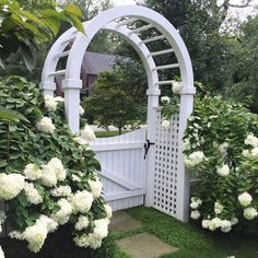 a white garden gate surrounded by flowers and greenery