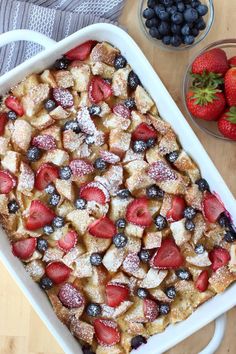 a casserole dish with berries and powdered sugar on top, next to bowls of strawberries