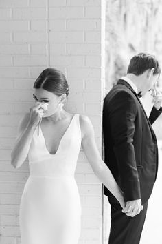 a bride and groom standing next to each other in front of a white brick wall