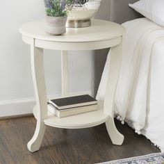 a white table with two books and a plant on it in front of a bed