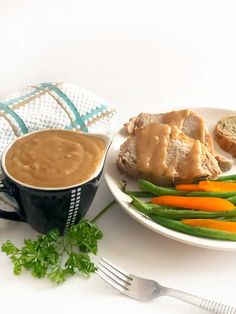 a white plate topped with meat and veggies next to a cup of sauce