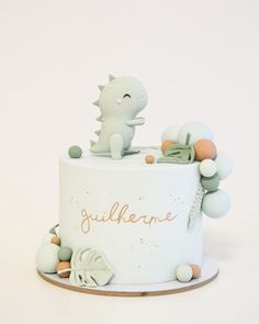 a white cake with a dinosaur on top and decorations around the edges that spell out gluhlenee